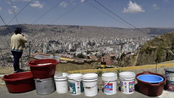 Una mujer espera la llegada de los camiones cisterna para poder llenar sus baldes en El Alto (AFP)