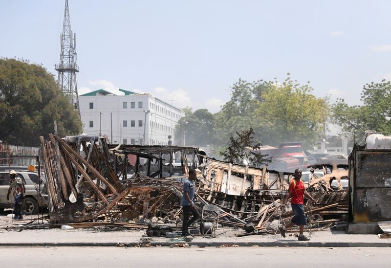 Varias personas caminan junto a restos de vehículos incendiados por bandas de delincuentes en Puerto Príncipe, Haití, el 25 de marzo de 2024 (REUTERS/Ralph Tedy Erol)