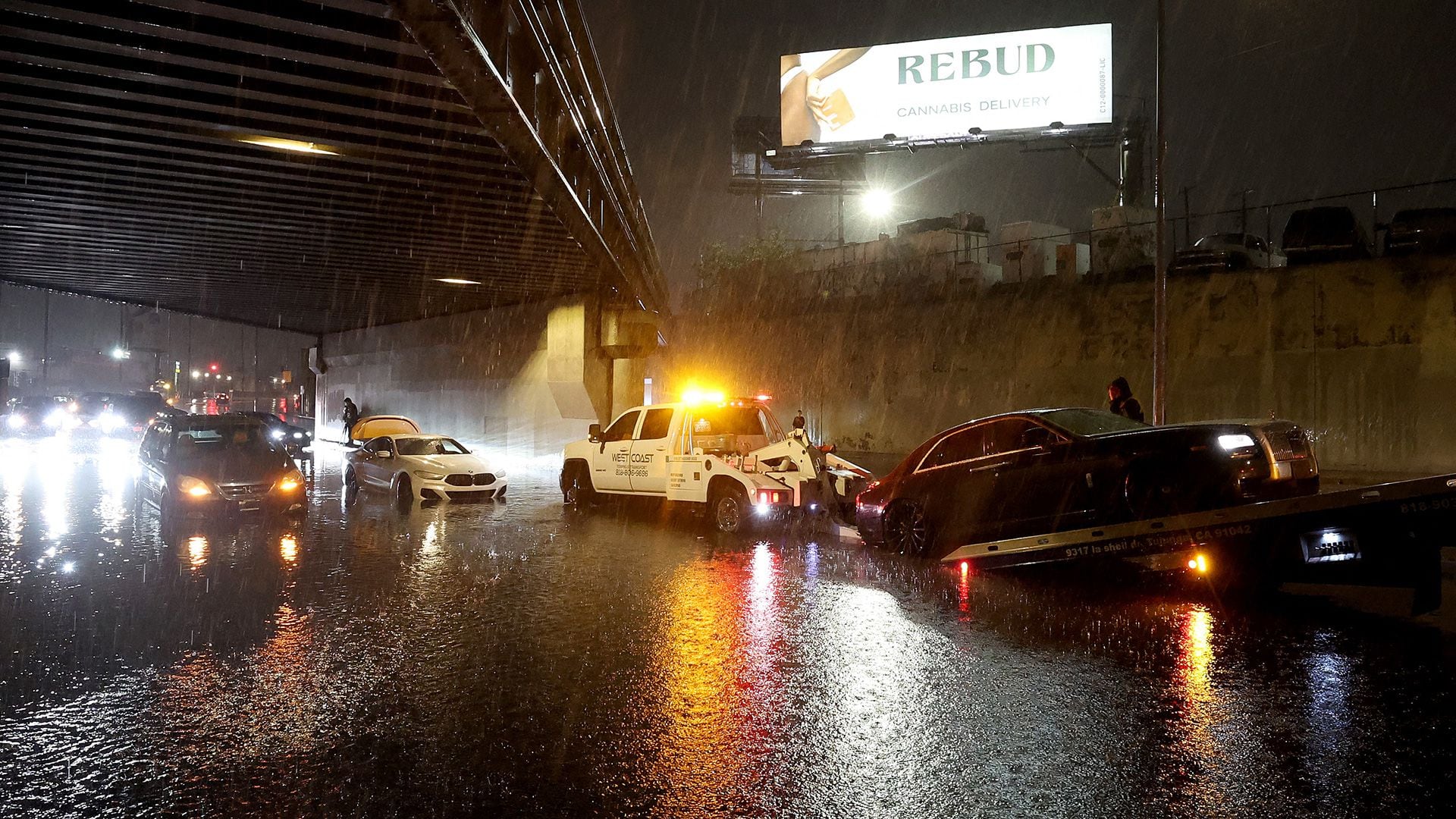 El conductor de una grúa saca autos varados de las inundaciones mientras la tormenta tropical Hilary avanza por el área en North Hollywood, California.