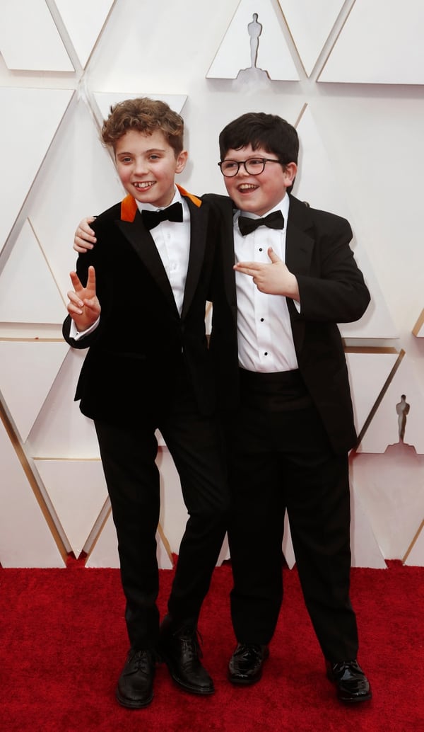 Roman Griffin Davis y Archie Yates, llegaron a la alfombra roja de los Oscar apostando al black tie con moño y camisa blanca. El distintivo fue el saco de Griffin Davis un detalle de chiffón naranja 