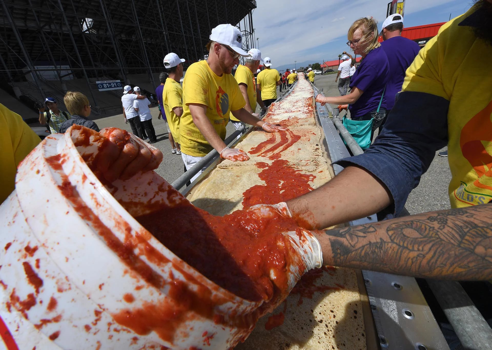 Volunteers spread tomato sauce and cheese onto the pizza base as they successfully break the Guinness World Records title for Longest pizza with a length of 1.32 miles (2.13km) at the Auto Club Speedway track, in Fontana, California on June 10, 2017.A consortium of pizza oven makers and bakers joined forces to shatter the previous record from held by Napoli in Italy by 600 feet(182 metres). / AFP PHOTO / Mark RALSTON