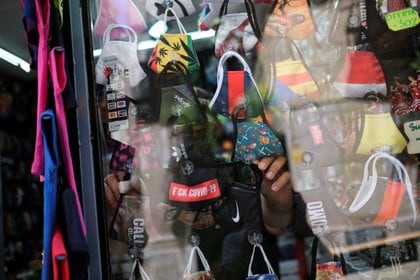 Un vendedor coloca una máscara facial para venderla a los turistas dentro de su tienda en el Barrio Gótico, en Barcelona (Reuters)