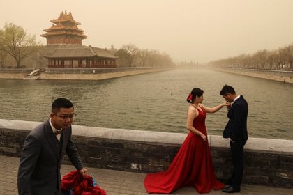La gente reacciona cuando se toman las fotos de su boda cerca de la Ciudad Prohibida, ya que la ciudad es golpeada por una tormenta de arena, en Beijing, China. REUTERS/Tingshu Wang