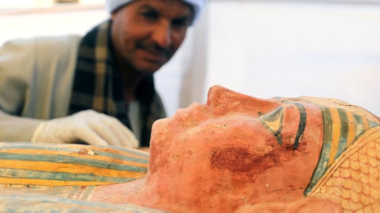 Un trabajador egipcio que inspecciona un sarcófago frente a la tumba faraónica recién descubierta (REUTERS)