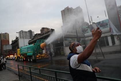 A man uses a mobile phone while a truck used in the mining industry sprays a mix of quaternary ammonium compounds and water to disinfect streets, amid the spread of the coronavirus disease (COVID-19) in Santiago, Chile May 12, 2020. REUTERS/Ivan Alvarado