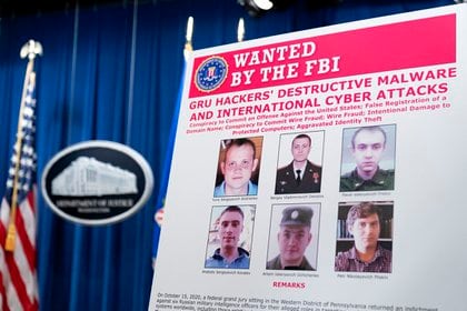 A poster showing six wanted Russian military intelligence officers is displayed before a news conference at the Department of Justice, Monday, Oct. 19, 2020, in Washington. (AP Photo/Andrew Harnik, pool)