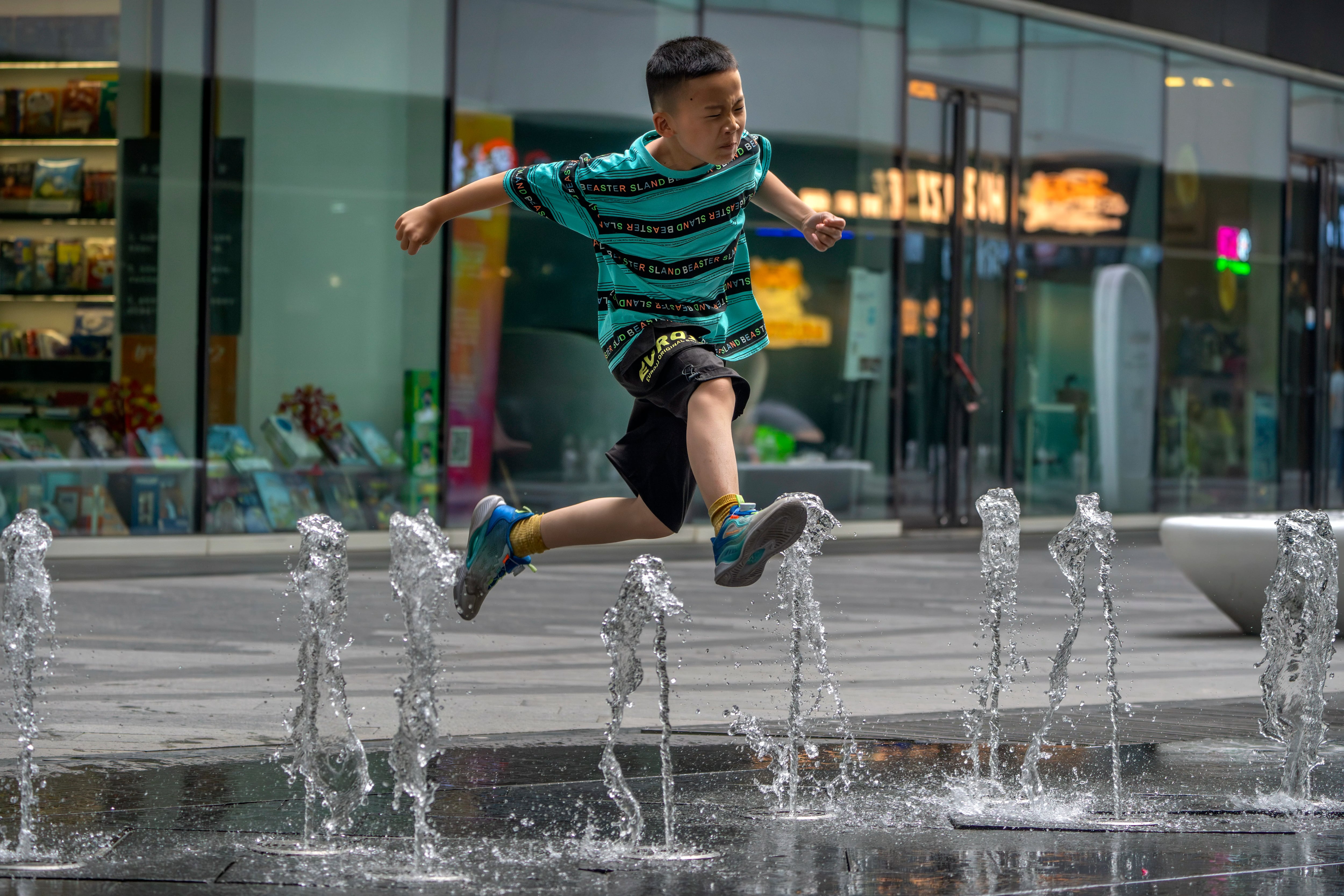 Un niño salta sobre una fuente en un complejo comercial y de oficinas en Beijing, el sábado 1 de julio de 2023 (AP Foto/Mark Schiefelbein)