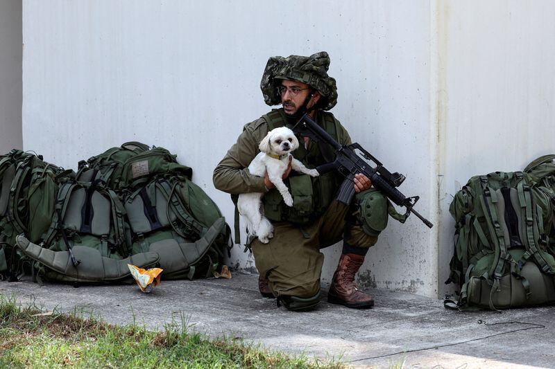 Un soldado israelí sostiene a un perro rescatado mientras toma posición cerca de un refugio antibombas en el kibutz Kfar Aza, en el sur de Israel. 10 de octubre de 2023 (Reuters/Ronen Zvulun)