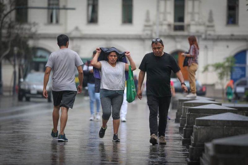Ciudadanos capitalinos caminan por la Plaza San Martín, en el Centro de Lima, momento después de que empezó una lluvia de mediana intensidad.