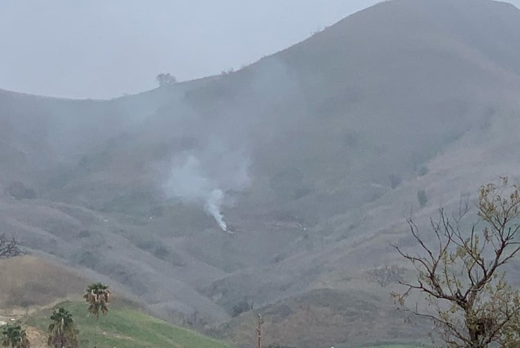 Una columna de humo crece desde el sitio en el que se estrelló el helicóptero, en las colinas al norte de Los Angeles (Reuters)