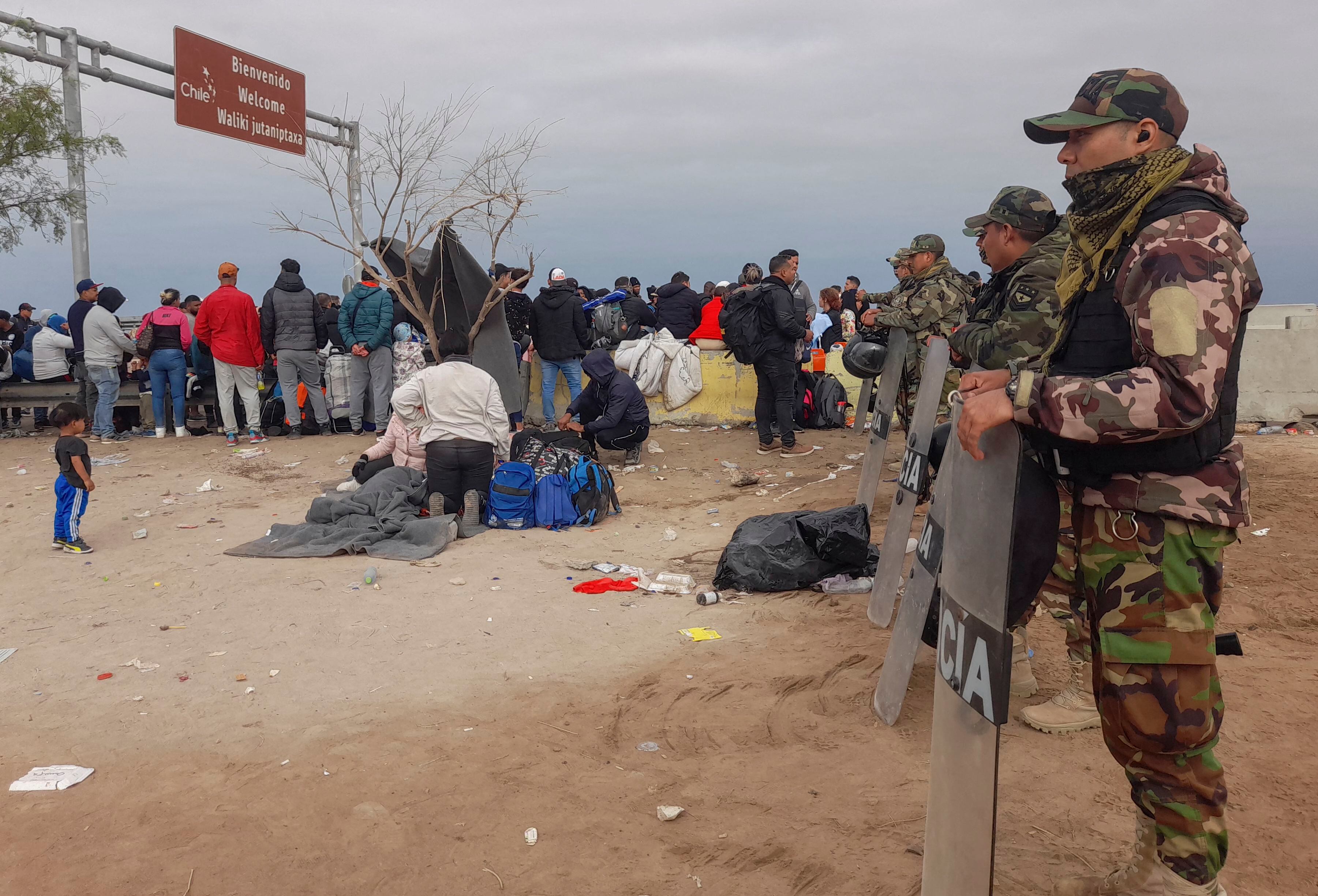Policías peruanos montan guardia en un campamento de migrantes de varias nacionalidades que permanecen varados en un desierto en la frontera entre Perú y Chile, el 26 de abril de 2023 (Javier Rumiche / AFP)