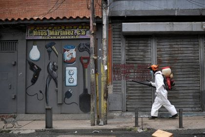 Un trabajador municipal esparce desinfectante en comercios cerrados en Caracas (AP)