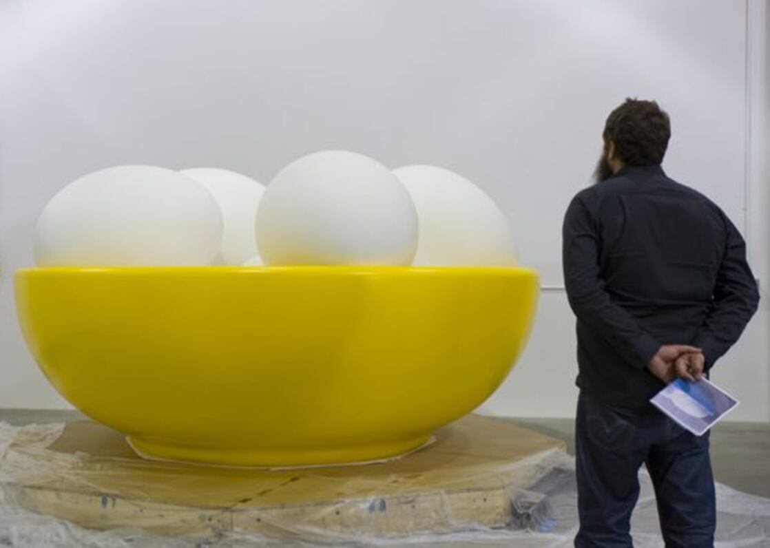 Una persona mira la escultura de Jeff Koons, Bowl With Eggs (Yellow), expuesta en Art Basel Miami Beach