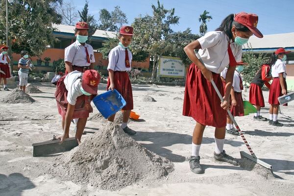 Estudiantes limpian un patio de su escuela, lleno de ceniza (Reuters)