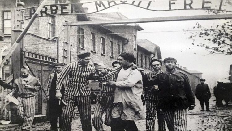 Asoman unas sonrisas. Algunos sobrevivientes luego de la liberación del Campo enmarcados por el cínico pórtico de Auschwitz: Arbeit macht frei (El trabajo los hará libres)