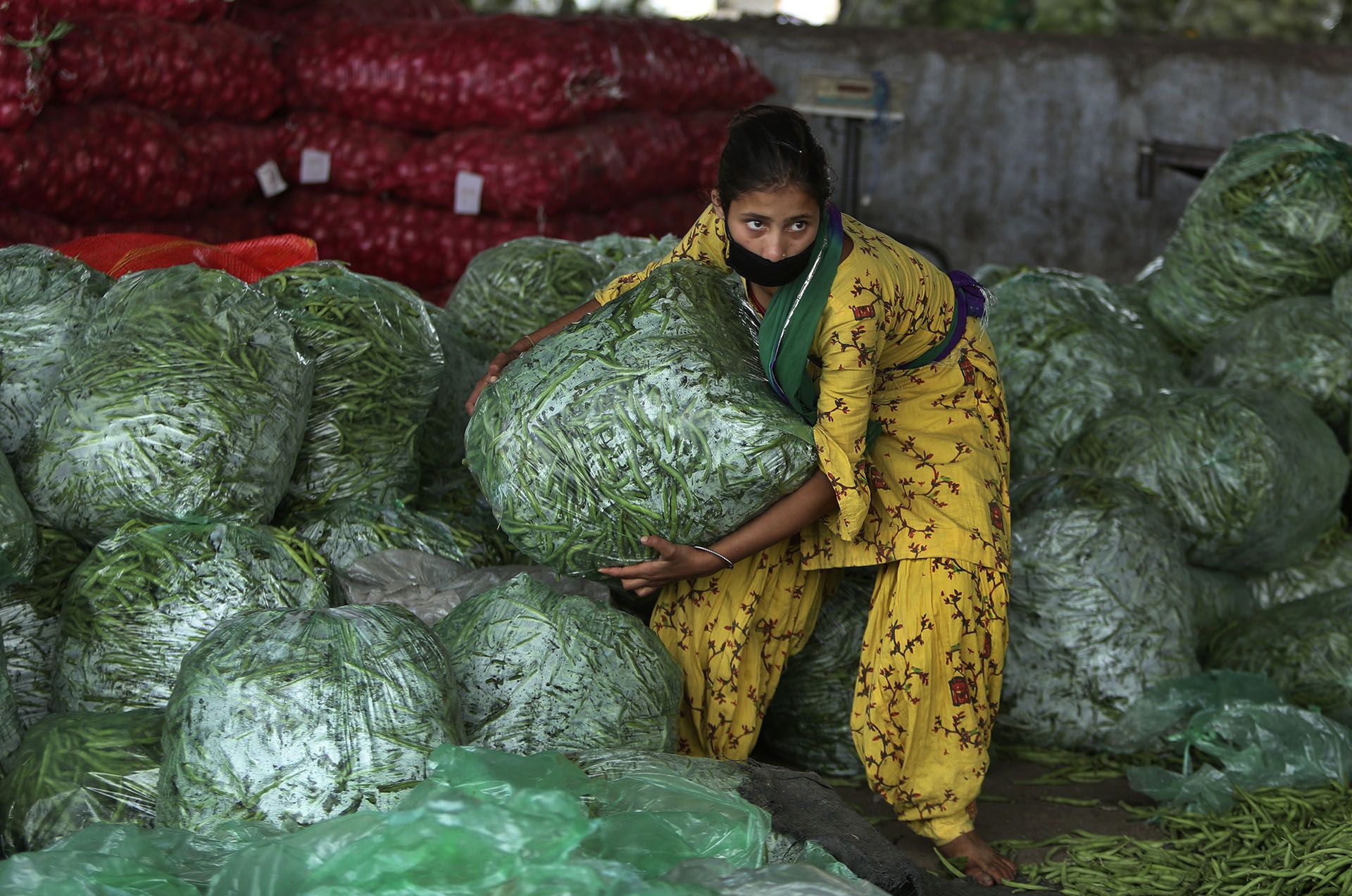 Una niña india trabaja en un mercado mayorista de verduras durante el cierre en Jammu, India, el lunes 20 de abril de 2020 (Foto AP/Channi Anand)