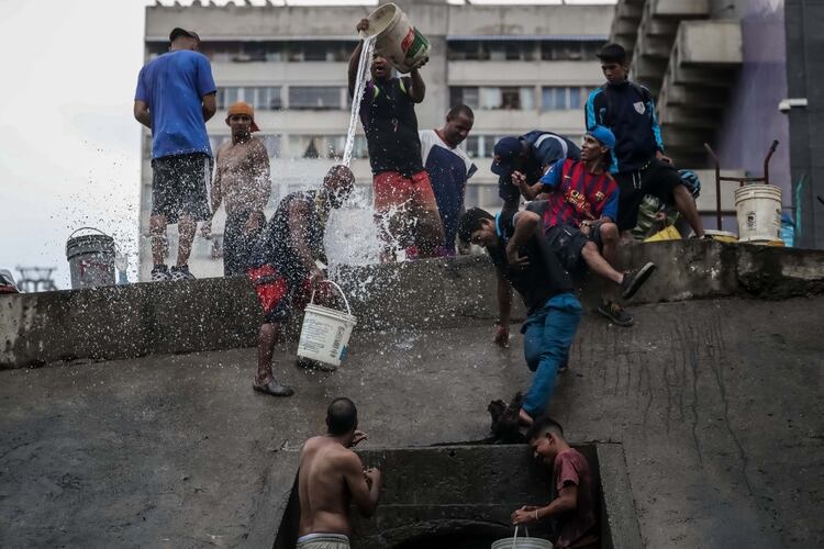 Un grupo de personas recoge agua de una tubería de desagüe en la orilla del Río Guaire, que atraviesa la ciudad y funciona como la vía principal de desagüe de las aguas residuales de la ciudad de Caracas (Venezuela). El suministro de agua ha quedado interrumpido en muchas partes del país como consecuencia de los sucesivos apagones que han afectado a Venezuela desde principios de marzo. (EFE)