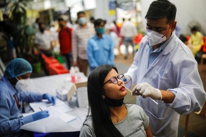 Un trabajador sanitario realiza un hisopado a una mujer en un centro médico de New Delhi, India (REUTERS/Adnan Abidi)
