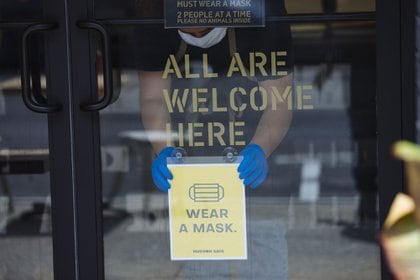 Un trabajador ajusta un letrero que pide a los clientes usar una máscara en una panadería y cafetería en Nueva York el 28 de junio.