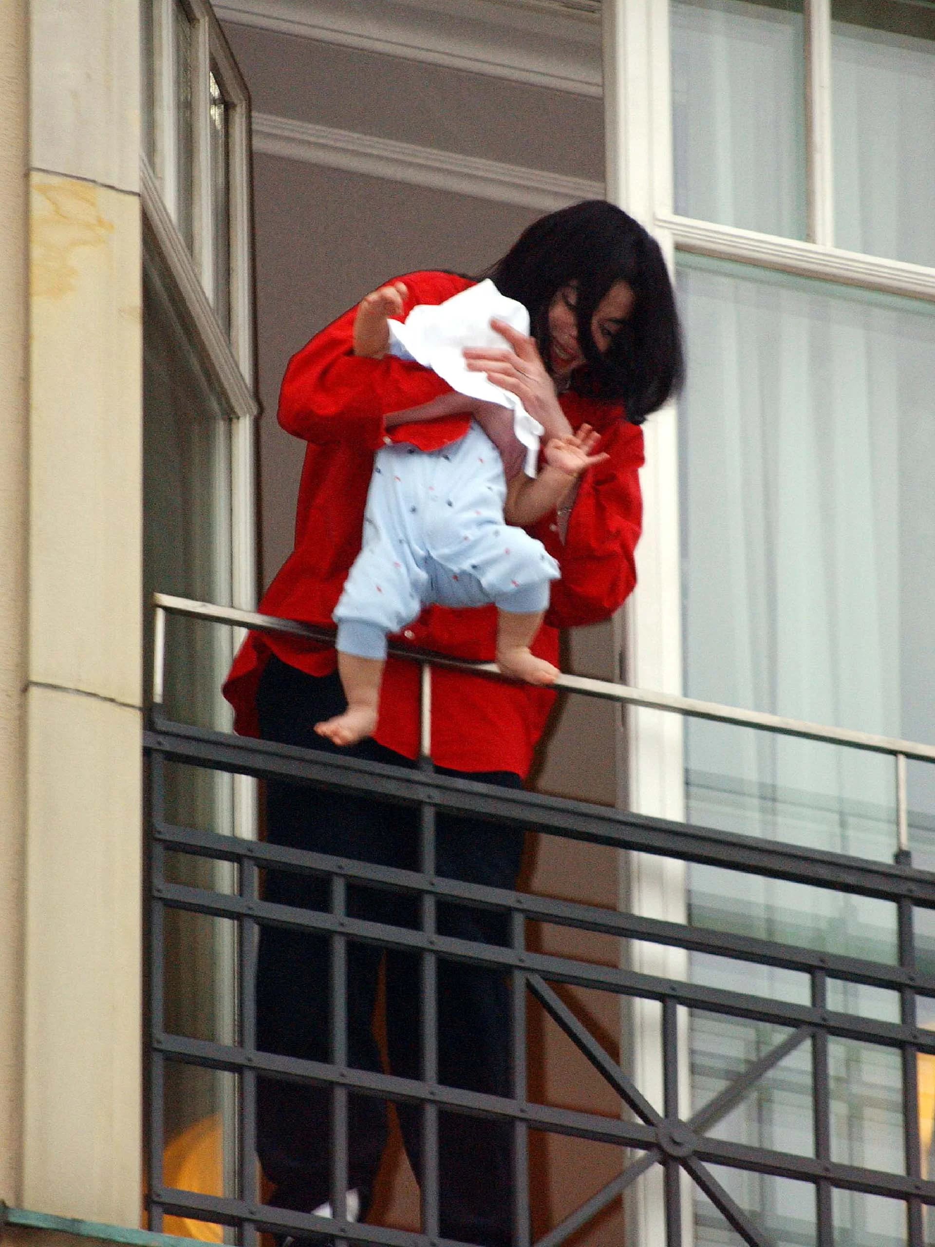 Michael Jackson sostiene peligrosamente a su bebé de ocho meses, Prince Michael II, en el balcón de un hotel en Berlín mientras saluda a los fans que fueron a vivarlo (Olaf Selchow/Getty Images)