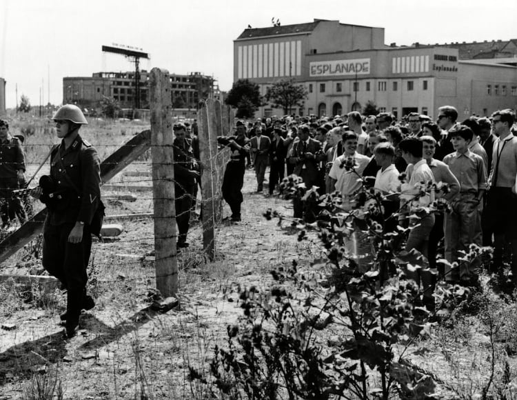 Un grupo de vecinos de Berlín Occidental observan a soldados orientales patrullando el alamabrado que caban de montar (Everett/Shutterstock)