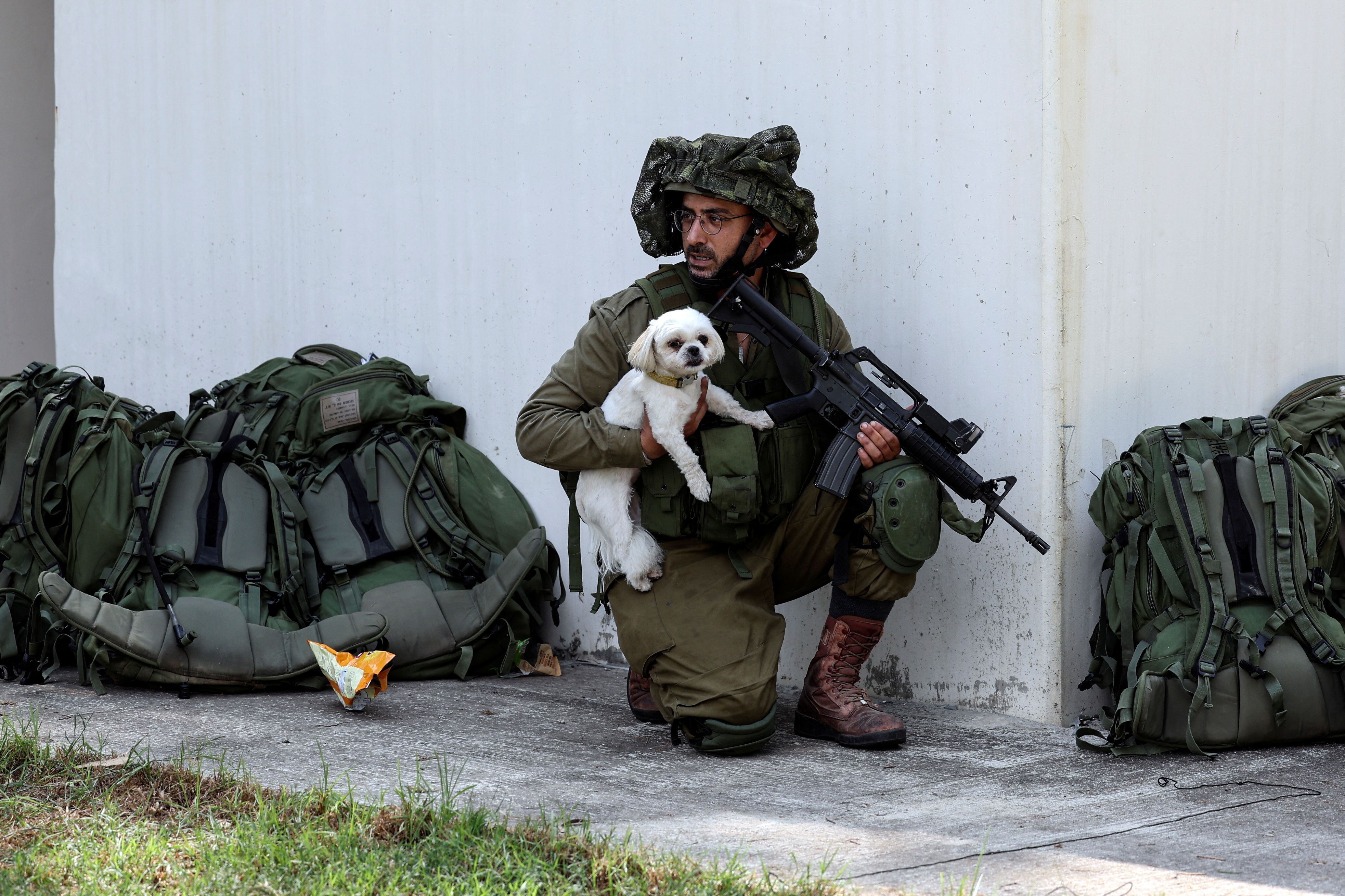 Un soldado israelí sostiene a un perro rescatado mientras toma posición cerca de un refugio antibombas en el kibutz Kfar Aza, en el sur de Israel, 10 de octubre de 2023 (Reuters)