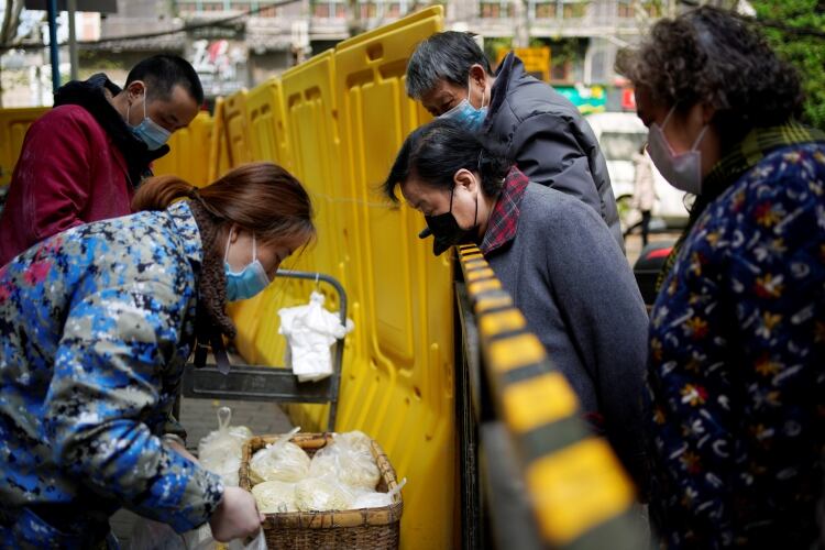 Residentes con máscaras compran a través de vallas amarillas que todavía bloqueaban en estos últimos días algunos bloques de apartamentos en Wuhan.