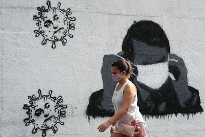 Una mujer pasa por delante de un grafiti que muestra al presidente de Brasil, Jair Bolsonaro, ajustando su máscara protectora, en medio del brote de coronavirus en Río de Janeiro el 2 de julio de 2020. REUTERS/Sergio Moraes