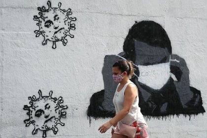 Foto de archivo. Una mujer pasa por delante de un grafiti que muestra al presidente de Brasil, Jair Bolsonaro, ajustando su máscara protectora, en medio del brote de la enfermedad coronavirus (COVID-19) en Río de Janeiro, Brasil. 2 de julio de 2020. REUTERS/Sergio Moraes