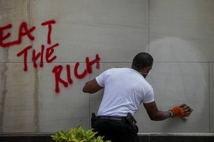 Una persona limpia una pared después de que los manifestantes la pintaron con aerosolcerca de la Casa Blanca, en Washington, durante los disturbios por la muerte de George Floyd. "Come a los ricos" se lee en la inscripción, firmada con el símbolo de los anarquistas (REUTERS / Tom Brenner)