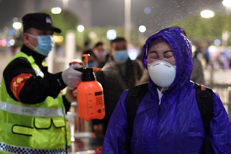 Un oficial de policía rocía desinfectante a una pasajera fuera de la estación de tren de Hankou después de que se levantaran las restricciones de viaje para abandonar Wuhan, la capital de la provincia de Hubei y el epicentro del nuevo brote de la enfermedad por coronavirus (Reuters)