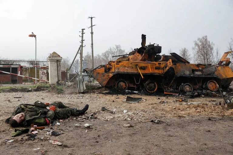  El cuerpo de un soldado ruso muerto yace en el suelo frente a un vehículo blindado ruso BTR-82 destruido, en la región  