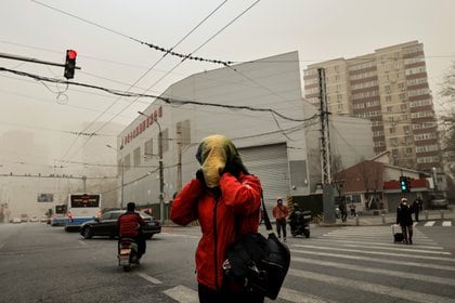 Una mujer cruza una calle con una cabeza cubierta en Beijing, China, mientras la ciudad está envuelta en bruma después de una tormenta de arena. REUTERS/Thomas Peter