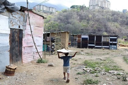 Un niño llevando una lámina de hojalata cerca de un grupo de casas hechas con barro, palos y hojalata levantadas en un terreno baldío en el que las familias se establecen porque no pueden pagar un alquiler, en el municipio de Sucre, cerca de Caracas (REUTERS/Manaure Quintero)