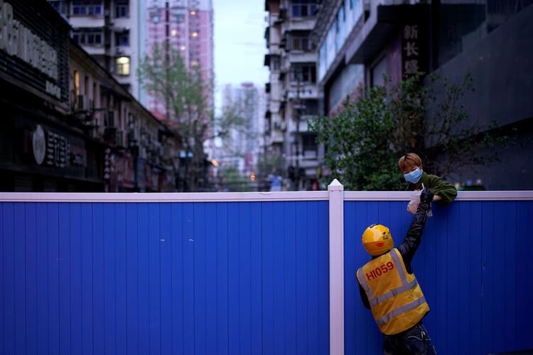 Un trabajador de reparto le pasa comida a una mujer sobre las barreras que bloquean la entrada a un área residencial en Wuhan, provincia de Hubei, el epicentro del brote de la enfermedad por coronavirus de China (COVID-19) (REUTERS)