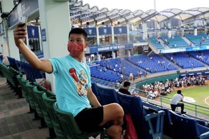 Un fanático del béisbol usa una máscara facial mientras se toma una selfie en el primer juego de la liga profesional que le permite al público desde el brote de COVID-19 en Taipei, Taiwán (Reuters)