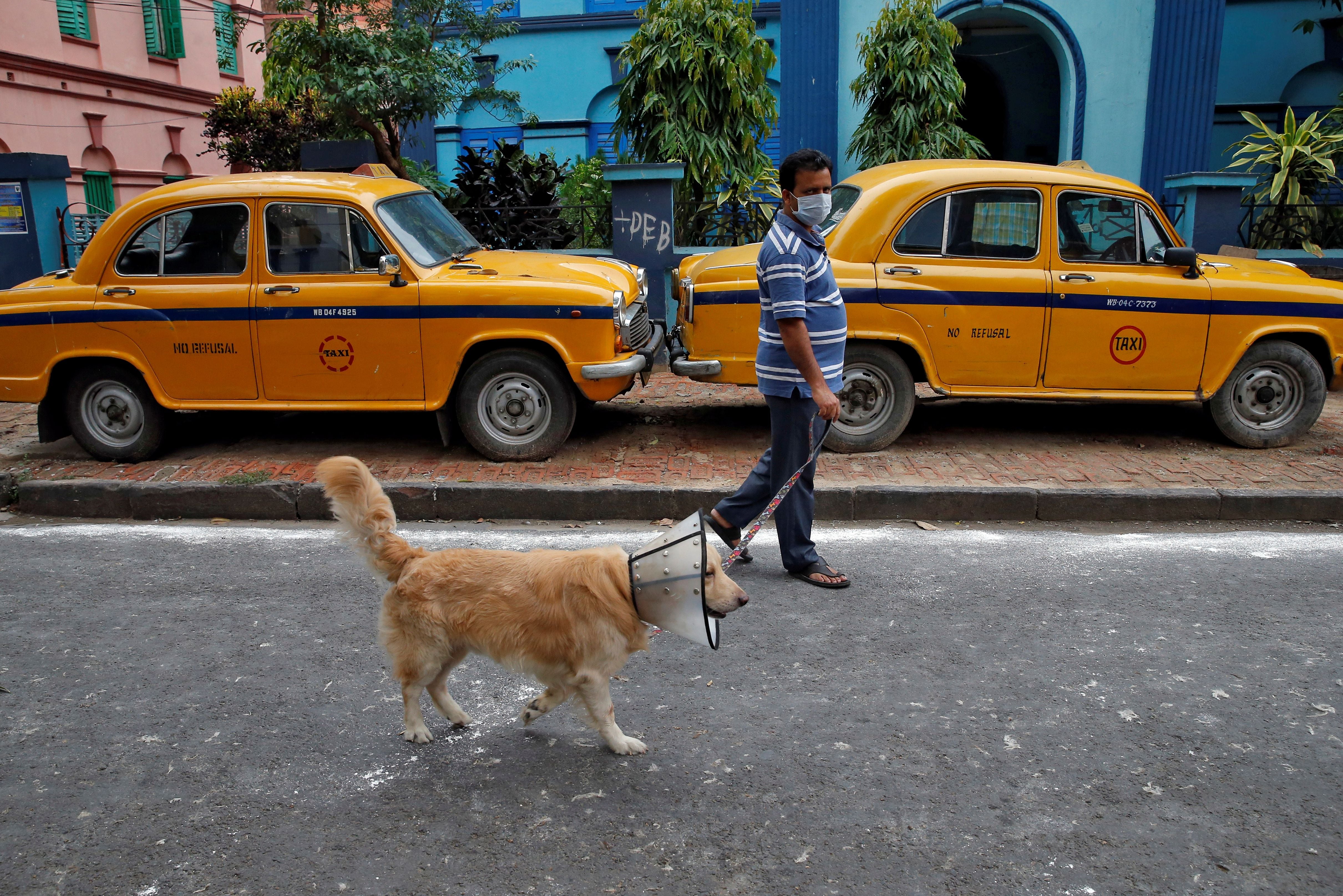 Un hombre con una máscara pasea a su perro con un collar isabelino, un dispositivo de protección para evitar que se lama el cuerpo, en Calcuta, India, el 24 de abril de 2020. REUTERS/Rupak De Chowdhuri