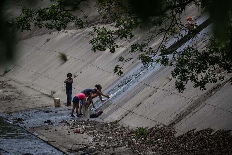 Un grupo de personas recoge agua de una tuberÃ­a de desagÃ¼e en la orilla del RÃ­o Guaire, que atraviesa la ciudad y funciona como la vÃ­a principal de desagÃ¼e de las aguas residuales de la ciudad de Caracas (Venezuela). EFE