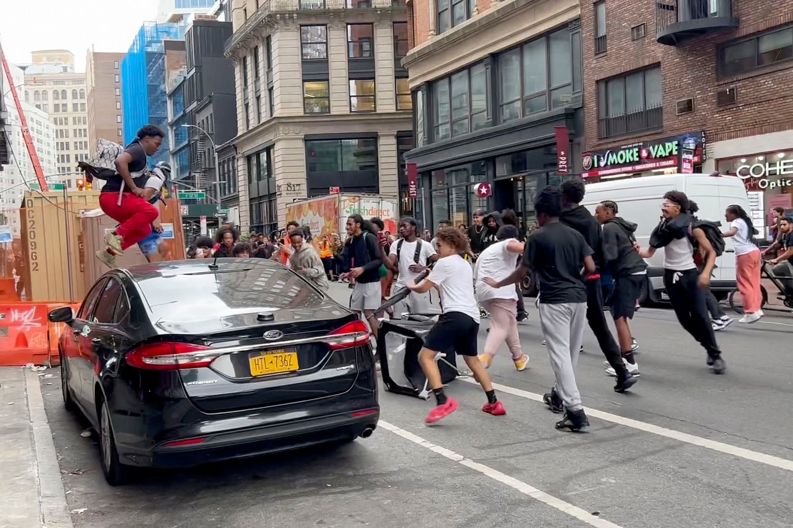 En este fotograma, un individuo salta sobre un auto mientras un grupo de personas corre por la calle en Broadway, cerca de Union Square, el viernes 4 de agosto de 2023 (AP Foto/Bobby Calvan)