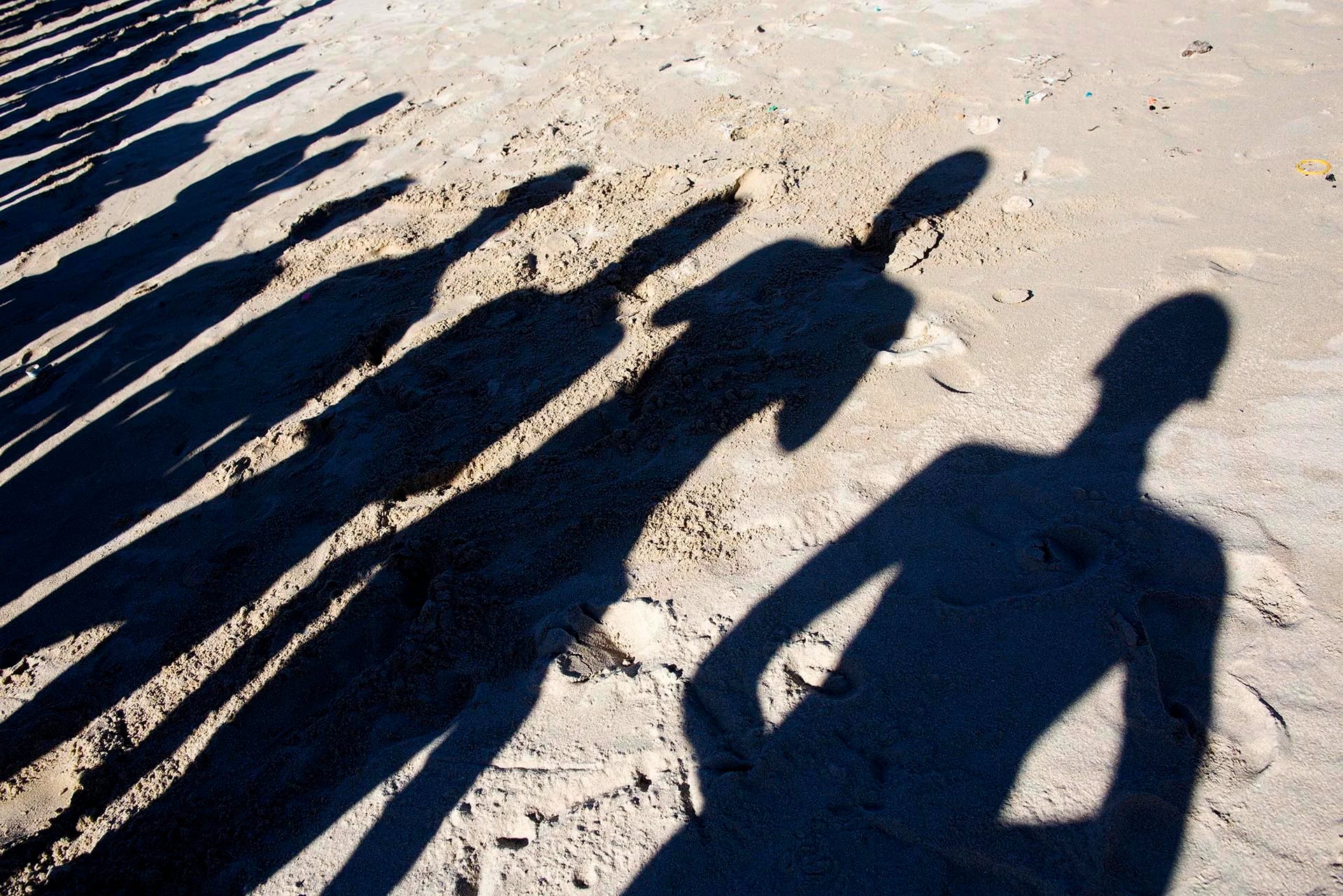 Sombras de jóvenes se proyectan en la arena mientras participan en una iniciativa para limpiar las playas con motivo del Día de la Juventud en Ciudad del Cabo, Sudáfrica