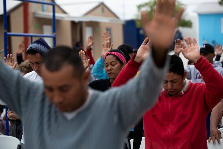 En esta imagen del 12 de octubre de 2019, decenas de cubanos oran en un refugio para migrantes en Reynosa, México. En años anteriores, los migrantes pasaban con rapidez por esta tierra de cárteles. Ahora, con las nuevas políticas migratorias de Estados Unidos, se quedan ahí durante meses mientras esperan sus citas en las cortes de la unión americana, varados en las fauces del crimen organizado. (AP Foto/Fernando Llano)