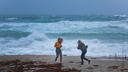 Brianna Thornberry, a la izquierda, y Savannah Johnson desafían a la tormenta en Palm Beach occidental, Florida, donde Isaías impacto con menor fuerza de la esperada. (Lannis Waters/The Palm Beach Post via AP)