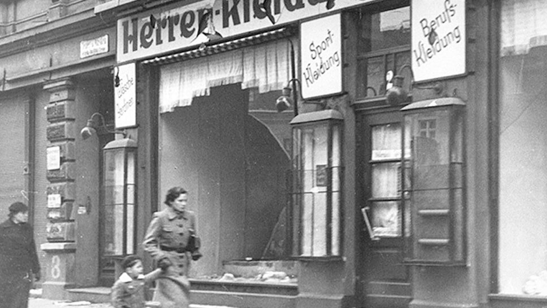 Una mujer con un niño pasan frente a la vidriera destrozada del negocio de un comerciante judío