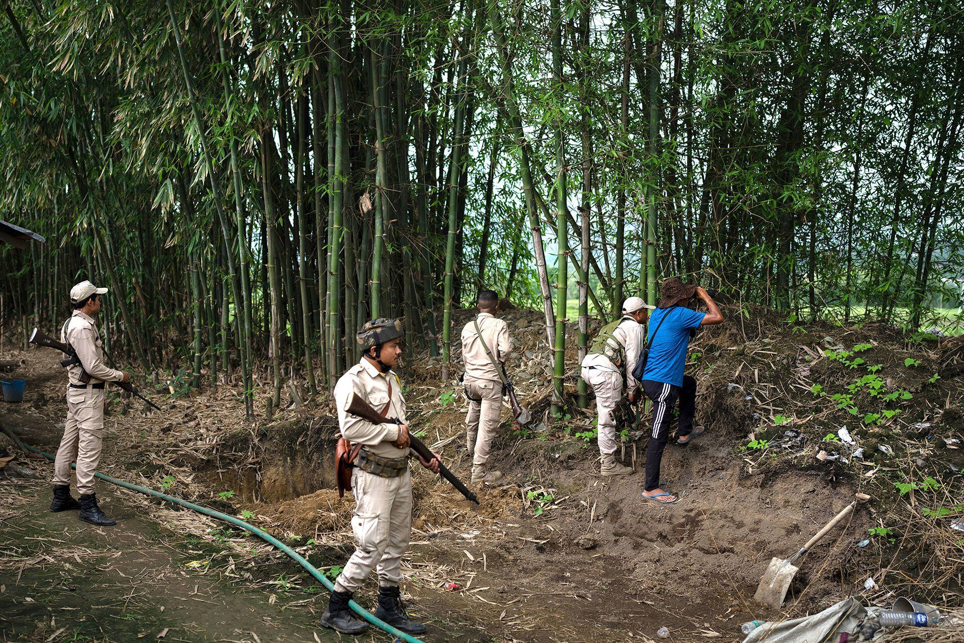 Policías de Manipur de la comunidad Meitei montan guardia como voluntarios, vestidos de azul, observan a través de binoculares las posiciones de los búnkeres de la comunidad tribal rival Kuki en Kwakta, a unos 50 kilómetros de Imphal, capital del estado nororiental indio de Manipur, el jueves 22 de junio de 2023 (Foto AP/Altaf Qadri)