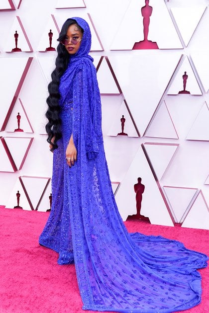 H.E.R impactó con su look en la alfombra roja con un total look azul íntegramente bordado. Una monoprenda de mangas largas con una capa con capucha. Completó su look con mini anteojos de sol y anillos 