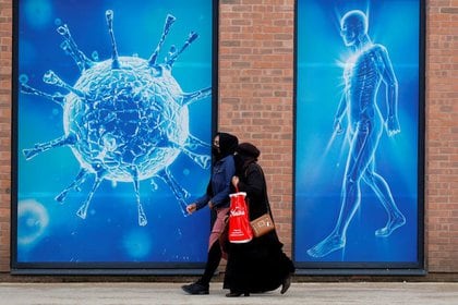 Dos personas caminan frente a una ilustración de un virus en el exterior de un centro científico regional en Oldham, Reino Unido,  REUTERS/Phil Noble