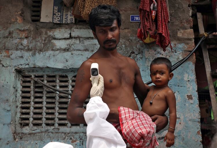 Un hombre sostiene a su hijo mientras un trabajador de la salud le toma la temperatura con un termómetro de infrarrojos en un área de tugurios de Calcuta, India, el 24 de abril de 2020. (REUTERS/Rupak De Chowdhuri)