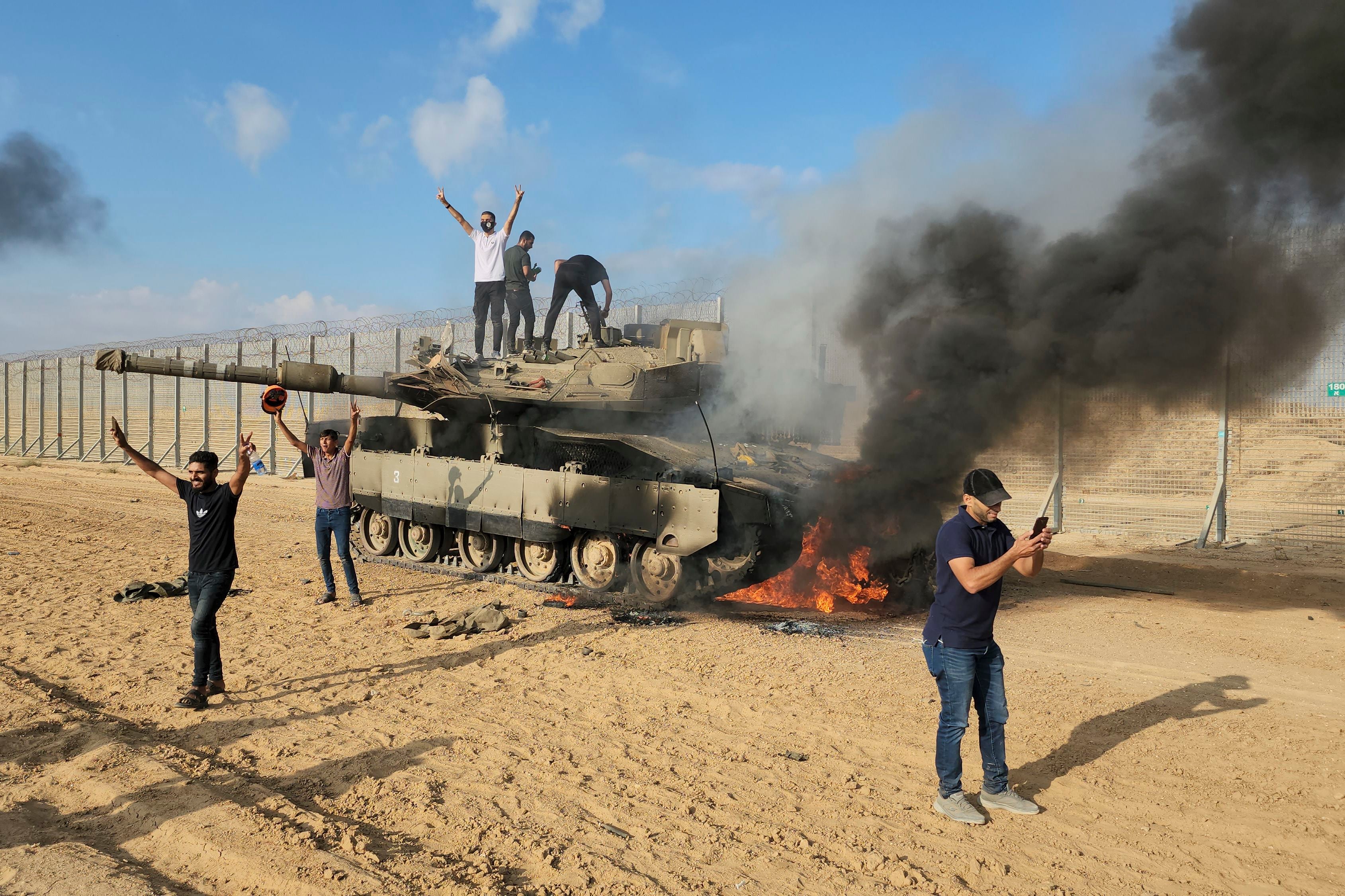 Palestinians celebrate next to a destroyed Israeli tank on the fence of the Gaza Strip, east of Khan Younis.  (AP Photo/Hassan Eslaiah)
