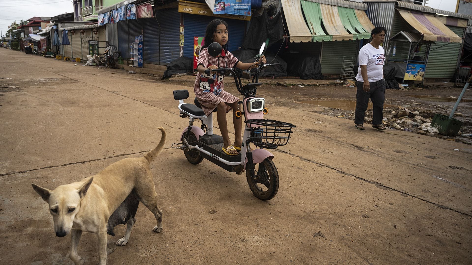 Una niña monta en bicicleta eléctrica por una carretera polvorienta, mientras un perro se aparta de su camino en el pueblo de Nakasong, junto al río Mekong, el 26 de agosto de 2022 en Si Phan Don, Laos (Getty Images)