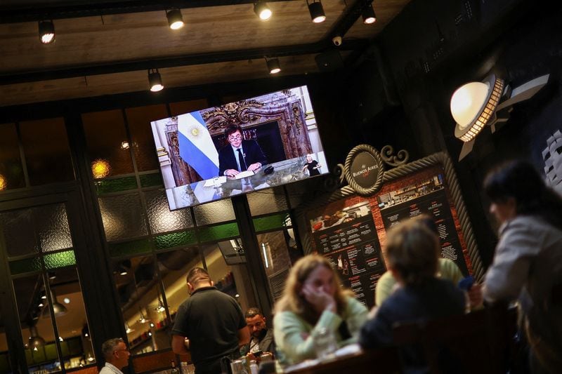 Una pantalla muestra al presidente Javier Milei, dando el discurso por cadena nacional por televisión, mientras varias personas cenan en un restaurante (REUTERS/Agustin Marcarian)
